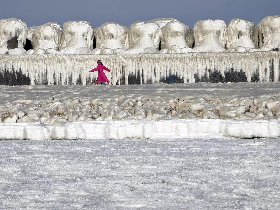 a girl runs past a wave protection dam covered in ice