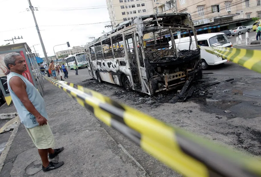 a man looks on at a damaged bus burned by drug traffickers