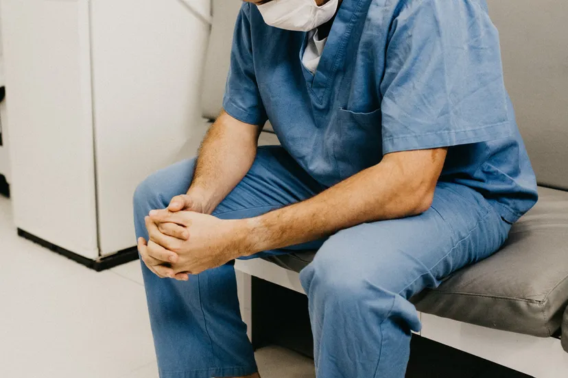 canva man wearing blue scrub suit and mask sitting on bench