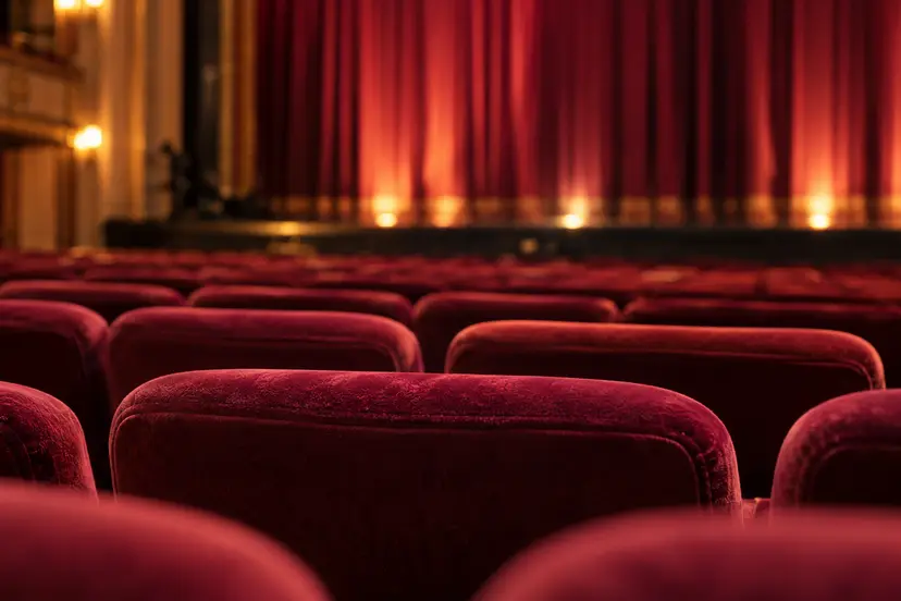 Rode theaterstoelen met een verlicht podium en gesloten gordijn op de achtergrond