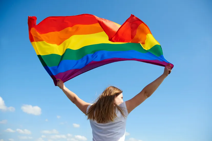 rear view of young woman waving rainbow flag