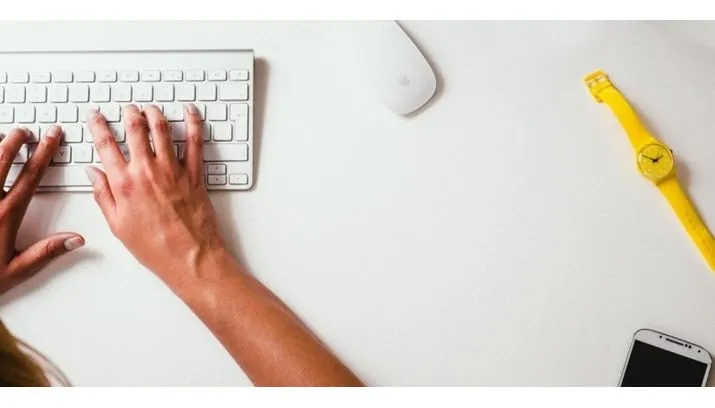 aerial view of hands on computer keyboards mobile phone and yellow watch on table
