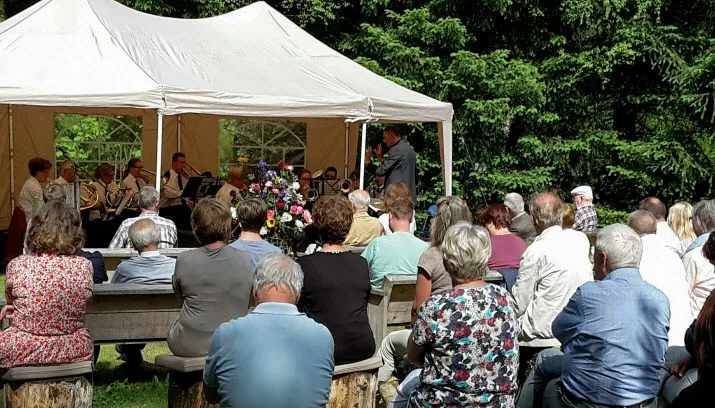 herinneringsbijeenkomst spelend orkest publiek en bloemstuk