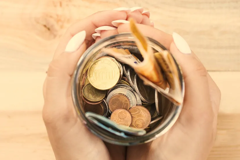 woman-s-hand-holding-saving-jar-against-wooden-background