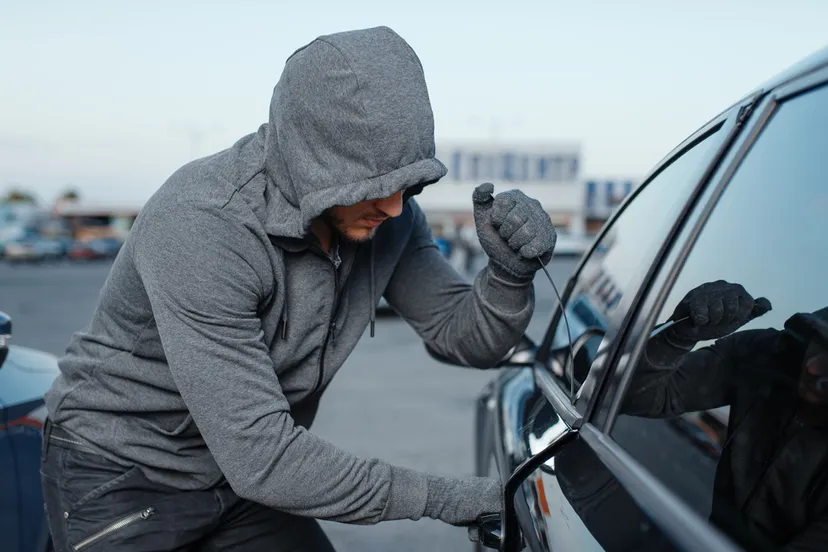 autodief die deurslot breekt criminele baan inbreker mannelijke rover met een kap die voertuig op parkeren opent