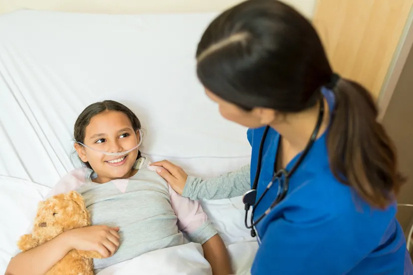 kleine meisjespatient die teddybeer vasthoudt terwijl hij tijdens de behandeling naar een gezondheidswerker op het ziekenhuisbed luistert