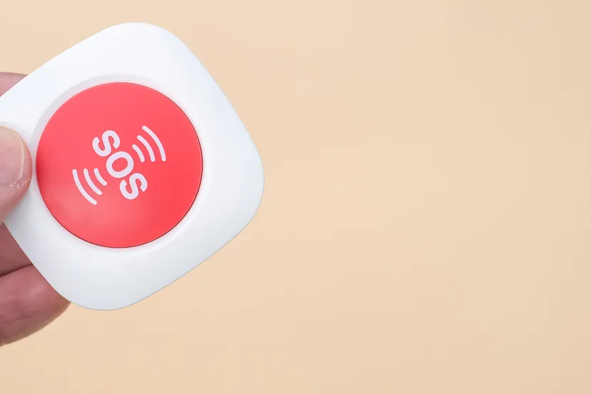 oudere hand met een draadloze sos noodalarmknop geisoleerd op lichtbruine achtergrond