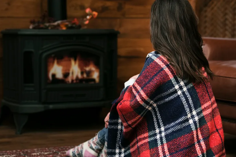 vrouw met deken naast brandende houtkachel