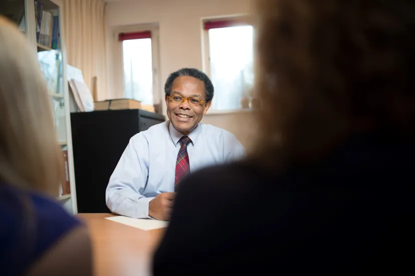 harry vriendelijk lachend aan bureau in gesprek met twee patienten