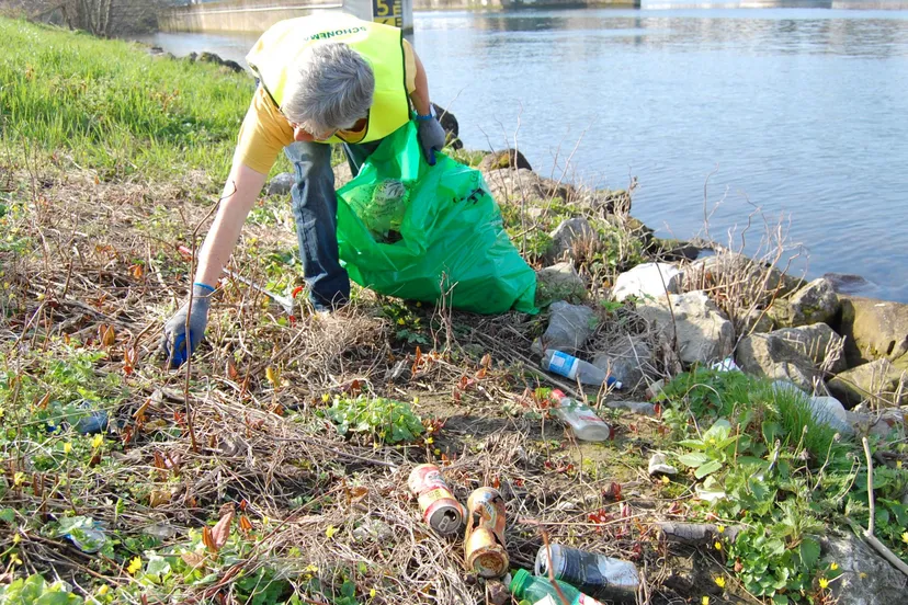 vrijwilliger ruimt afval op aan maasoever
