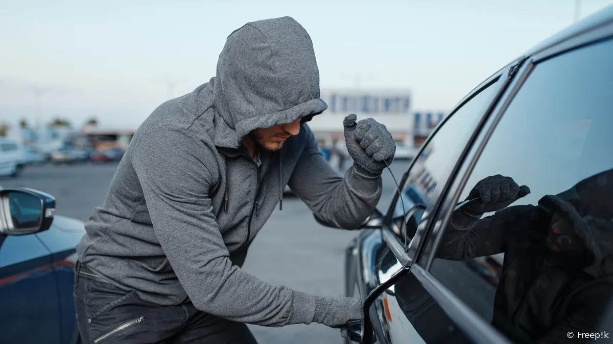 autodief die deurslot breekt criminele baan inbreker mannelijke rover met een kap die voertuig op parkeren opent