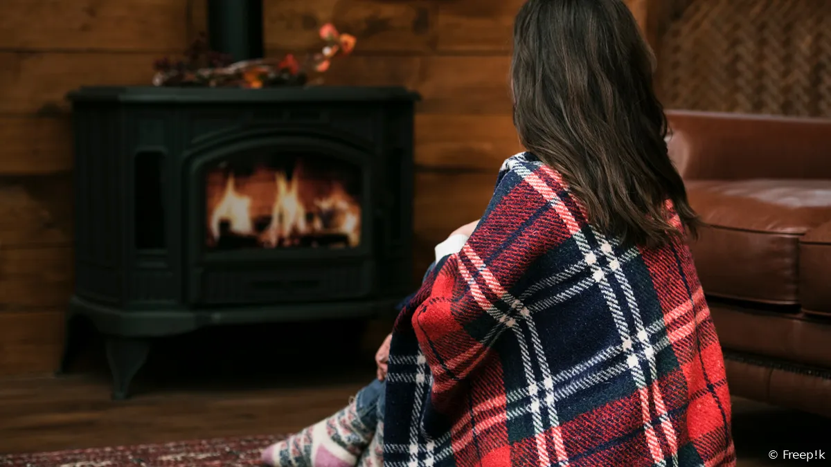 vrouw met deken naast brandende houtkachel