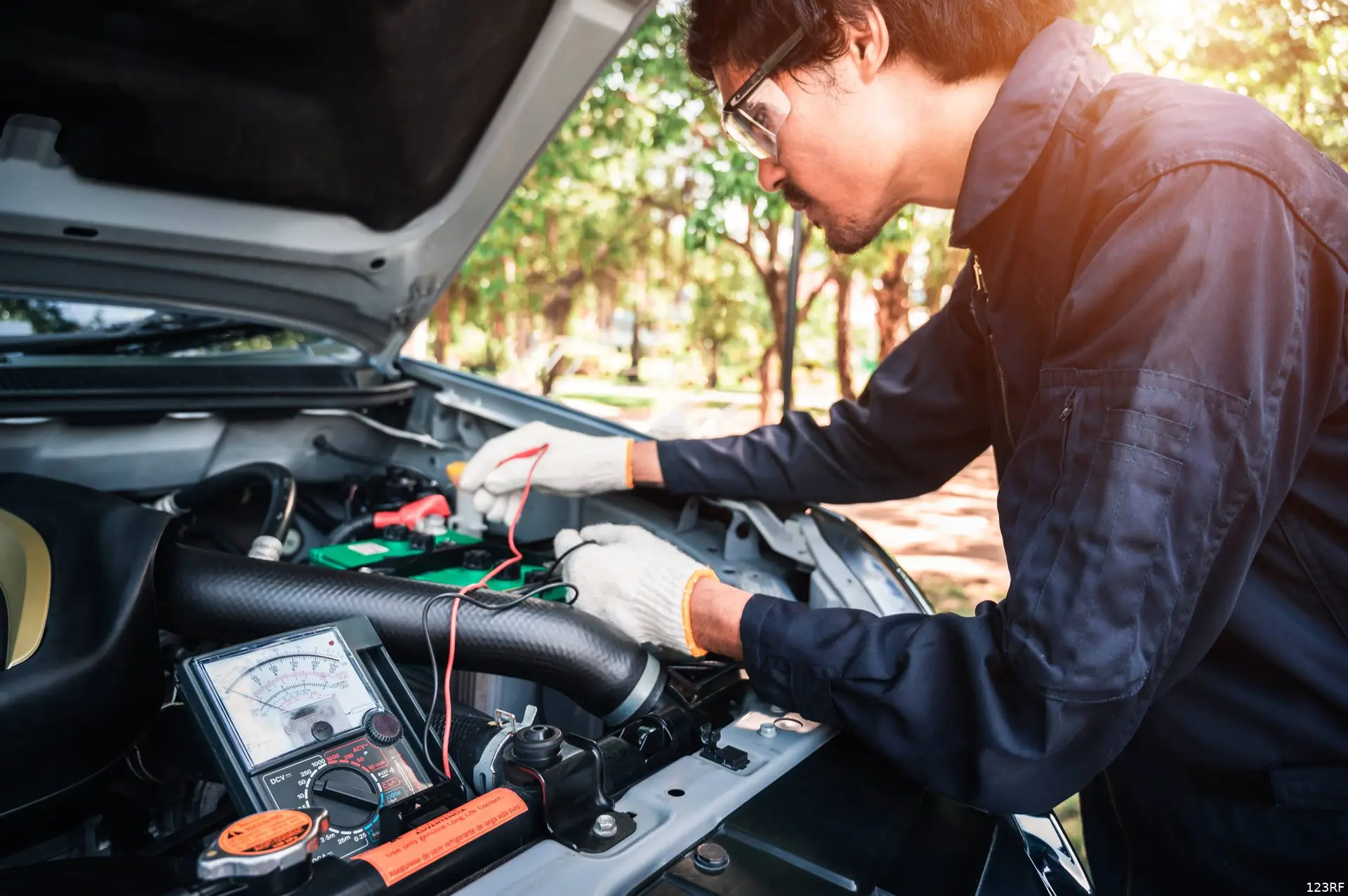 Een monteur meet met een accutester de spanning van een auto-accu onder de geopende motorkap.