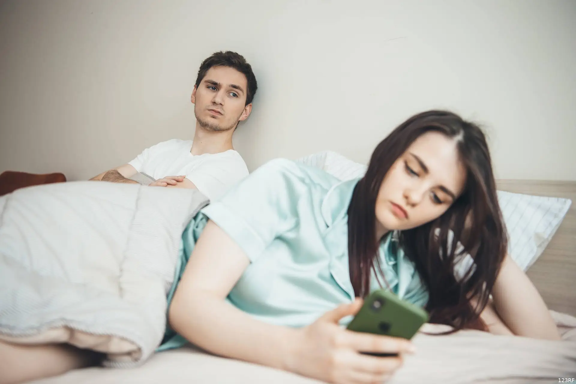 Een man en een vrouw liggen 's avonds in bed en kijken op hun telefoon.