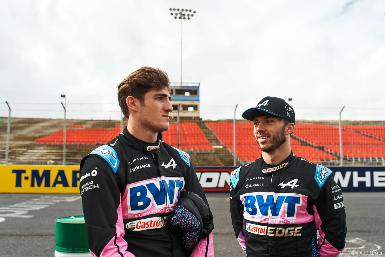 Jack Doohan stands next to Pierre Gasly, chatting during an Alpine marketing event, both dressed in their racing suits.