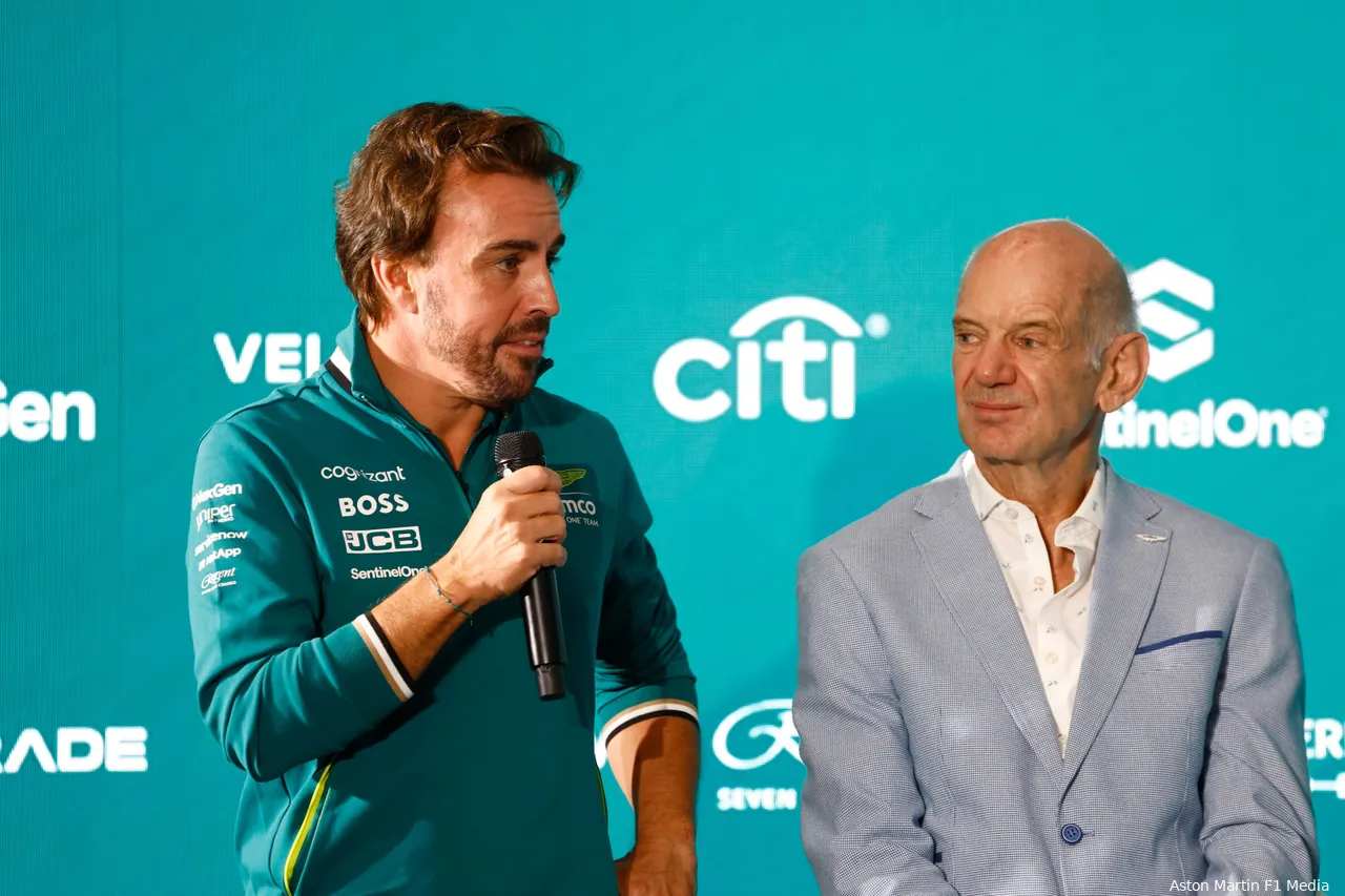 Fernando Alonso speaking to the media with Adrian Newey beside him at an Aston Martin press conference, partner logos in the background.