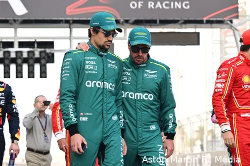 Fernando Alonso walks alongside Lance Stroll in team racing suits, with Alonso's hand resting on Stroll's shoulder, sharing a moment of camaraderie.