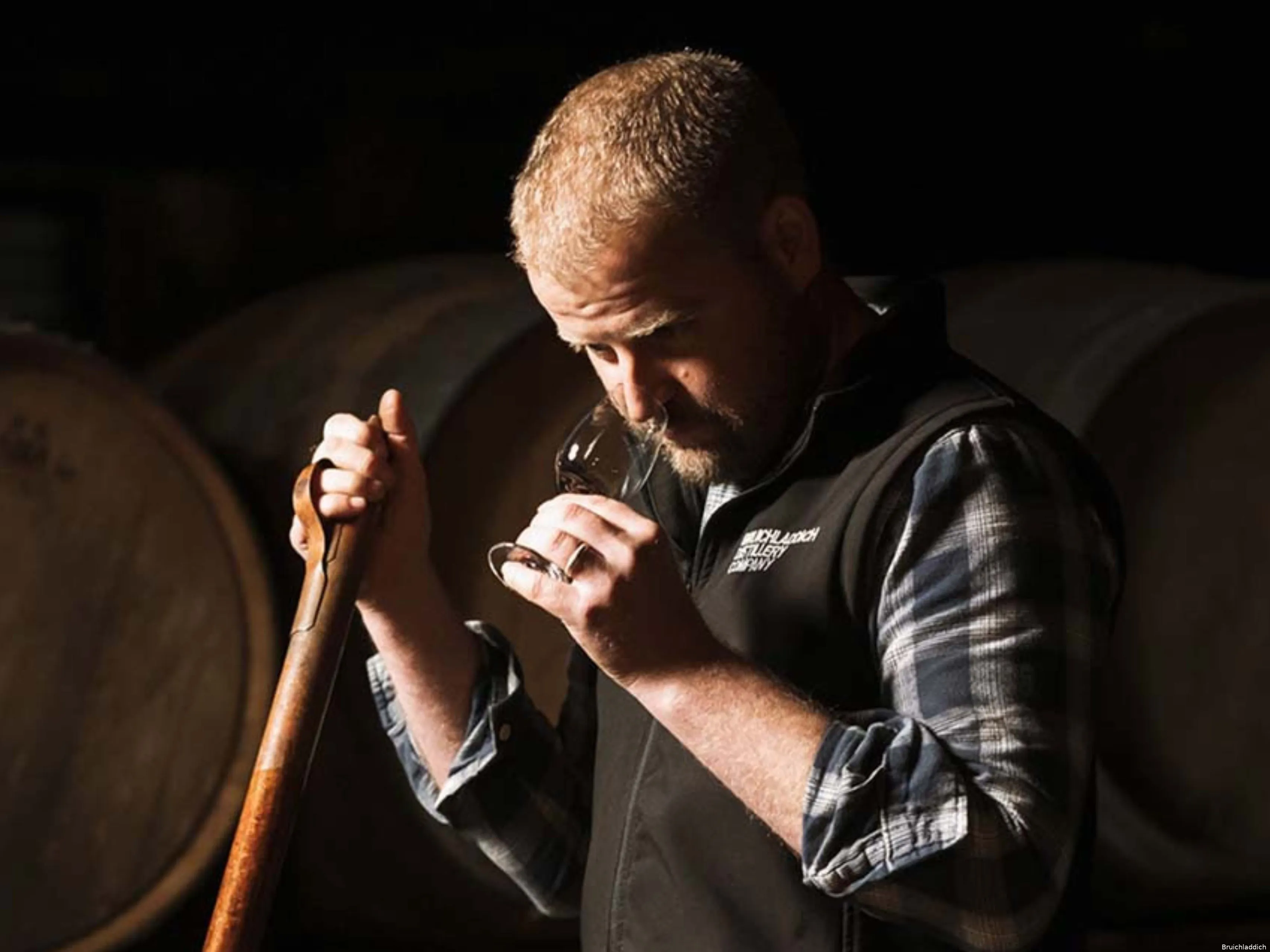Adam Hannett Bruichladich Distillery Octomore Farm met een Tulip Glass naast whiskyvaten