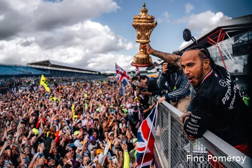 Lewis Hamilton celebrates with British fans on track at Silverstone Circuit after winning the 2024 British Grand Prix, raising the trophy above his head with one hand.