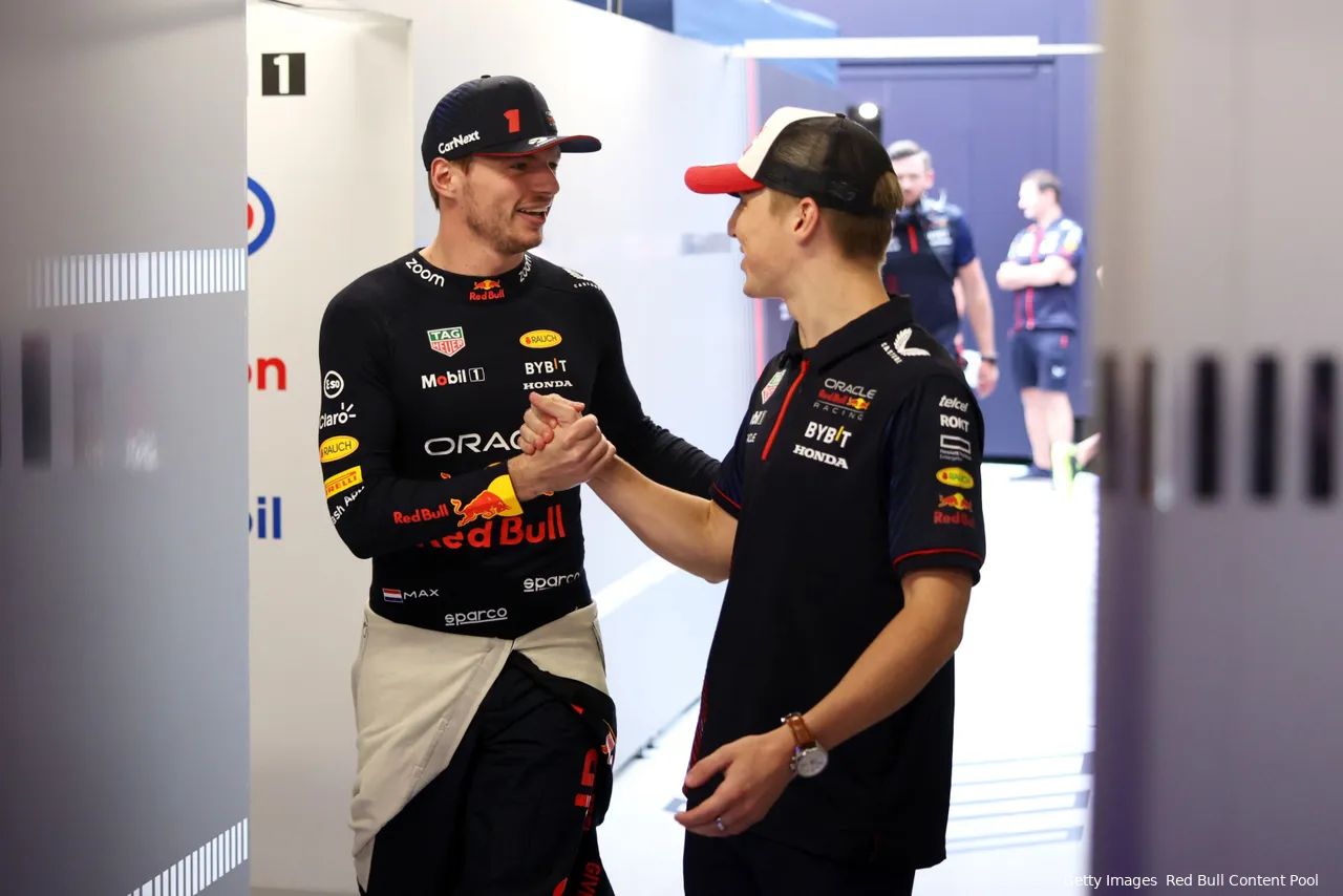 Max Verstappen and Liam Lawson, dressed in Red Bull team attire, shaking hands and chatting inside the team's hospitality area.