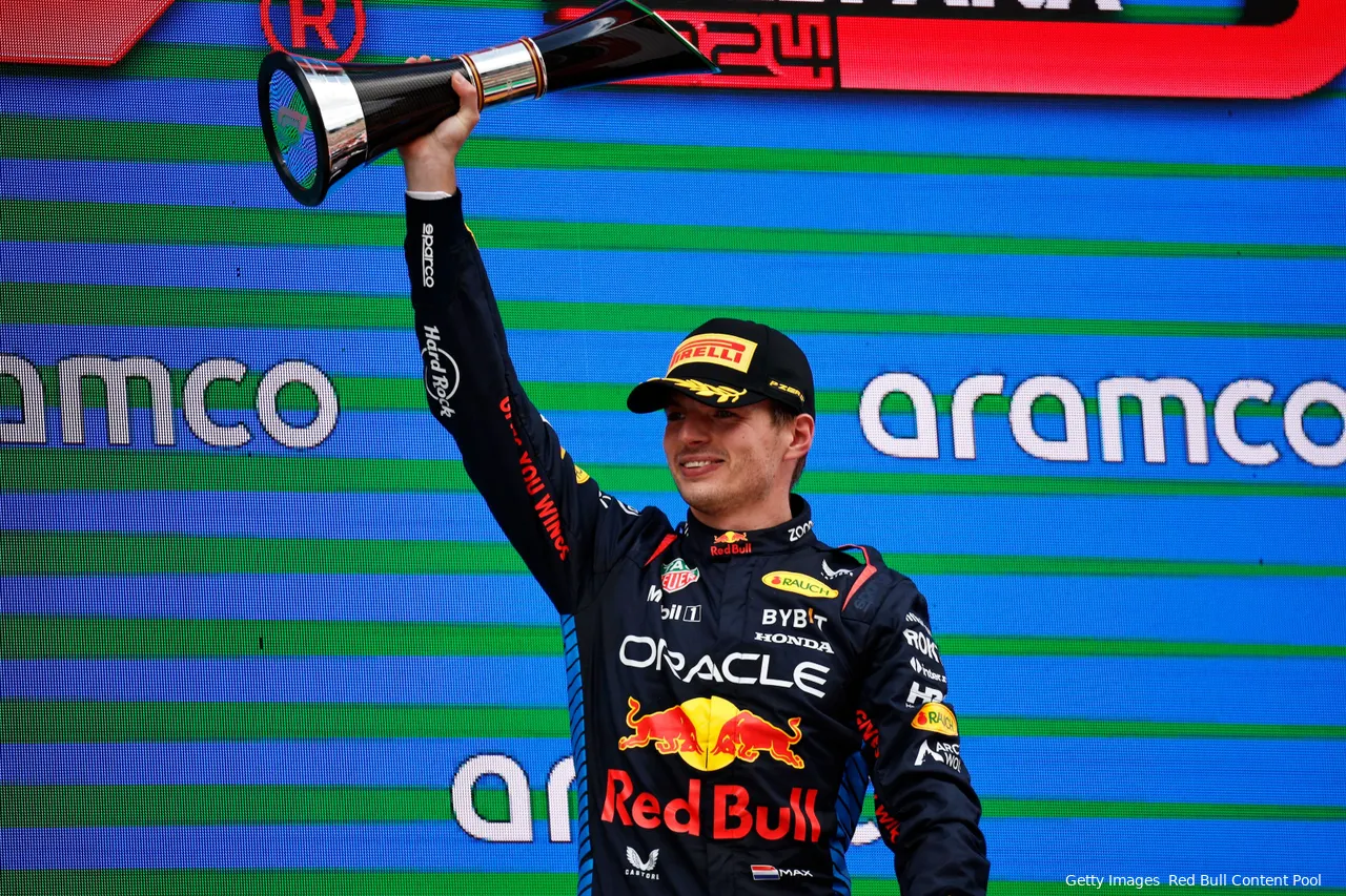 Max Verstappen smiling while holding the winner's trophy for the 2024 Spanish Grand Prix high above his head with his right hand.