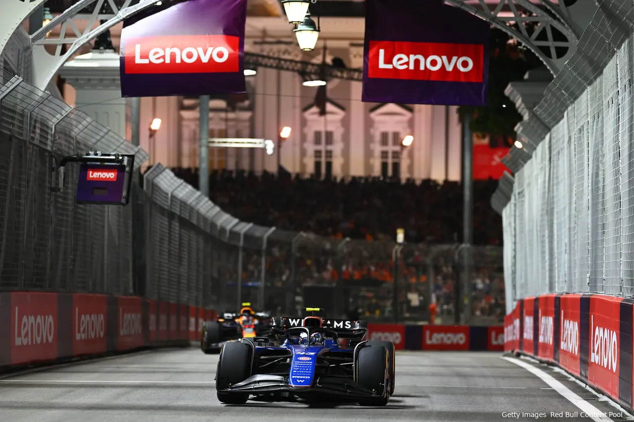 Franco Colapinto in his Williams leading Sergio Perez in a Red Bull, who struggled to overtake. Walls on both sides and grandstands in the background.