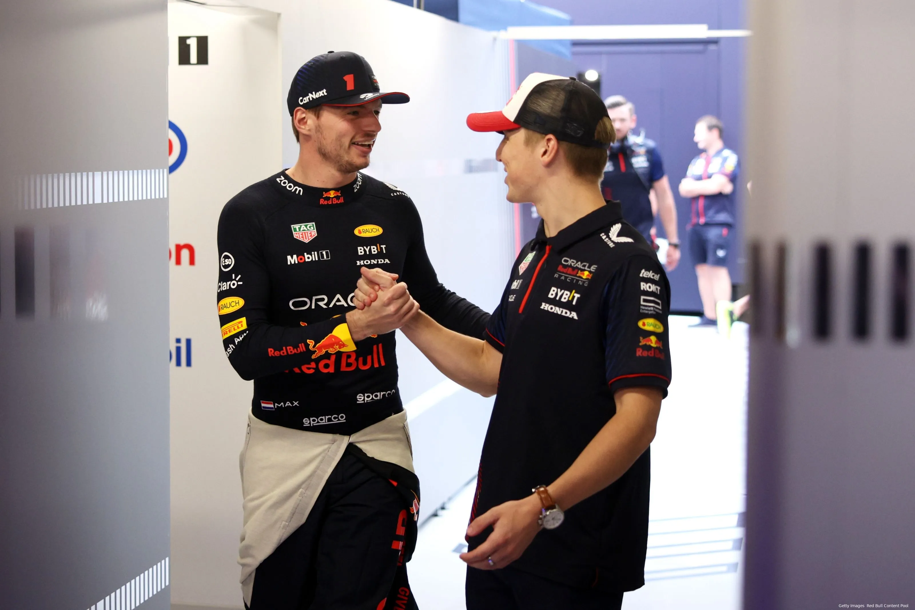 Max Verstappen and Liam Lawson, dressed in Red Bull team attire, shaking hands and chatting inside the team's hospitality area.
