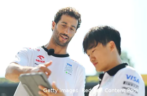 Daniel Ricciardo and Yuki Tsunoda standing in the pit lane at Monza Circuit, both intently looking at the screen of a tablet.