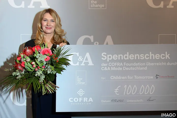 Steffi Graf holding flowers in left hand and cheque in another for a charity.