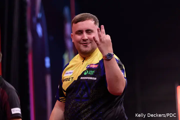 Luke Littler raises several fingers.