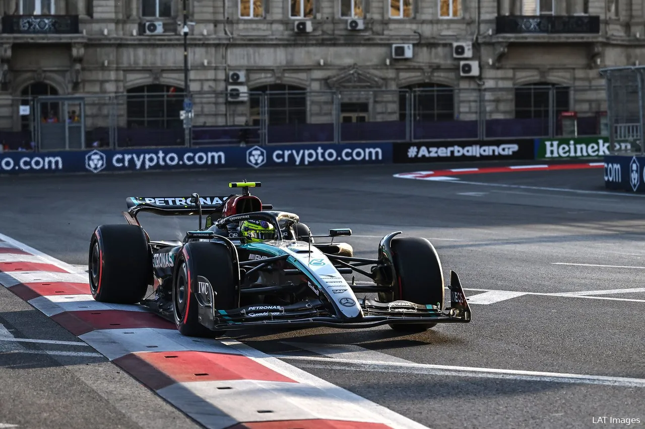 Lewis Hamilton on a flying lap with soft tires, exiting a corner and running over the red and white curb at Baku City Circuit, with track barriers and city buildings in the background.