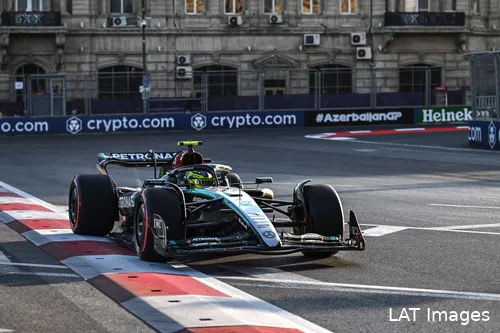 Lewis Hamilton on a flying lap with soft tires, exiting a corner and running over the red and white curb at Baku City Circuit, with track barriers and city buildings in the background.