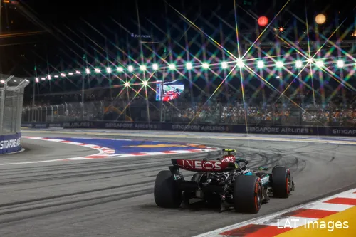 Back of Lewis Hamilton's car approaching a left-hand corner at Marina Bay Street Circuit during the Sunday night race, with grandstands and floodlights in the background.