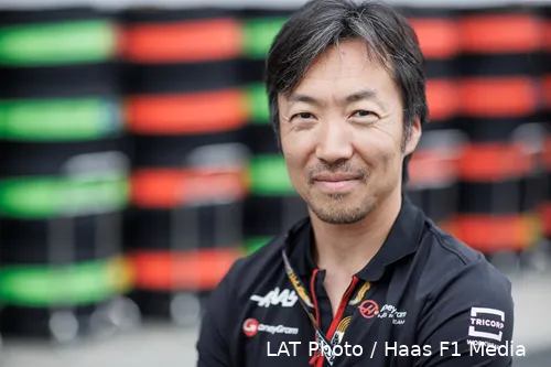 Haas F1 team principal Ayao Komatsu smiling at the camera during an official photoshoot in team uniform with a blurred background.