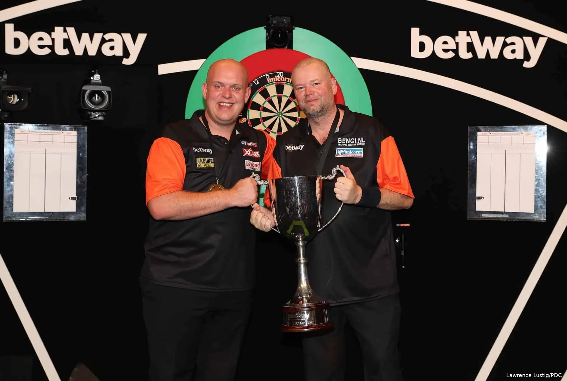 Michael van Gerwen en Raymond van Barneveld houden de trofee omhoog na het winnen van de World Cup of Darts.