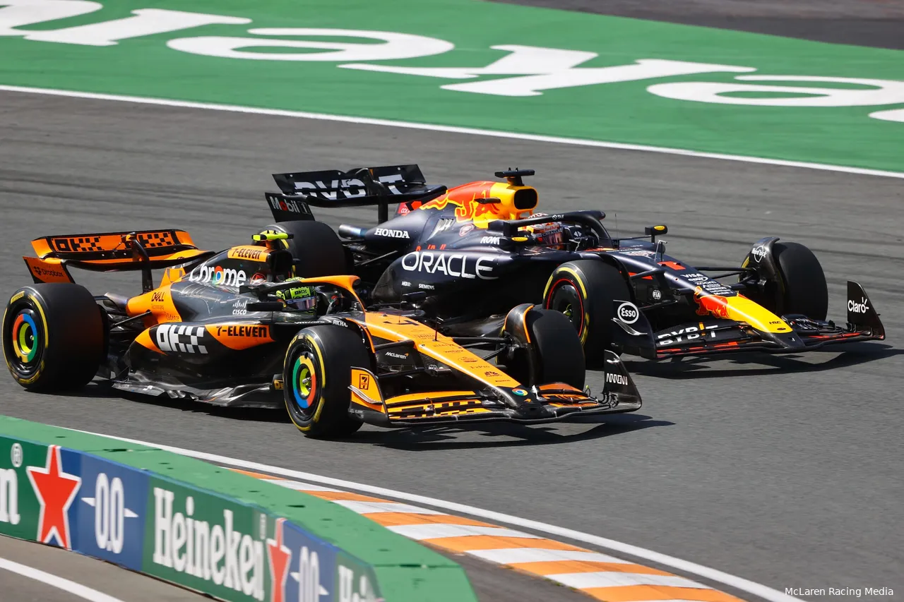 Lando Norris, in a McLaren car, overtaking and driving side by side with Max Verstappen in a Red Bull car at the first corner of Circuit Zandvoort.