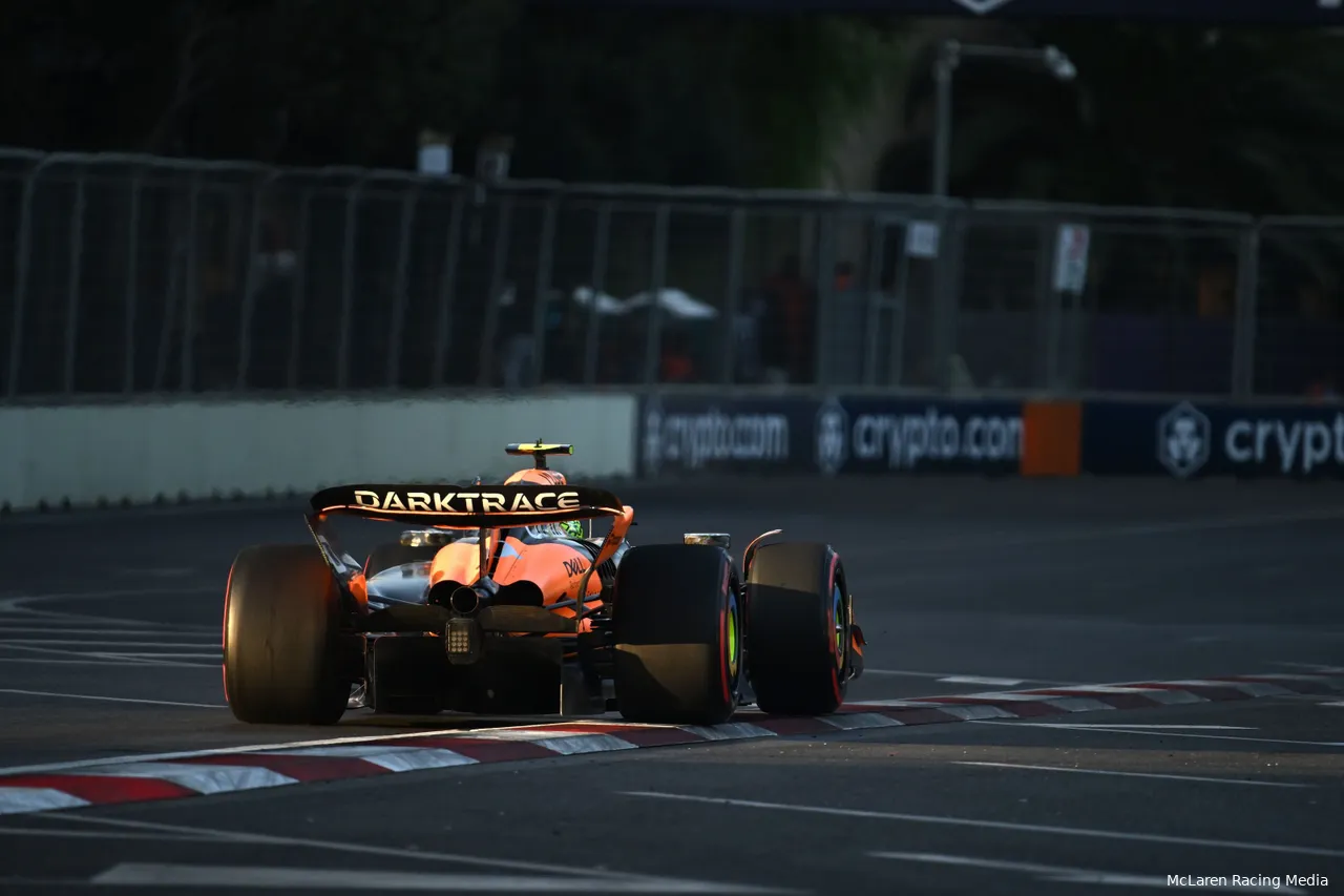 Rear view of Lando Norris's car exiting turn 16 at Baku City Circuit during golden hour, with track barriers in the background.