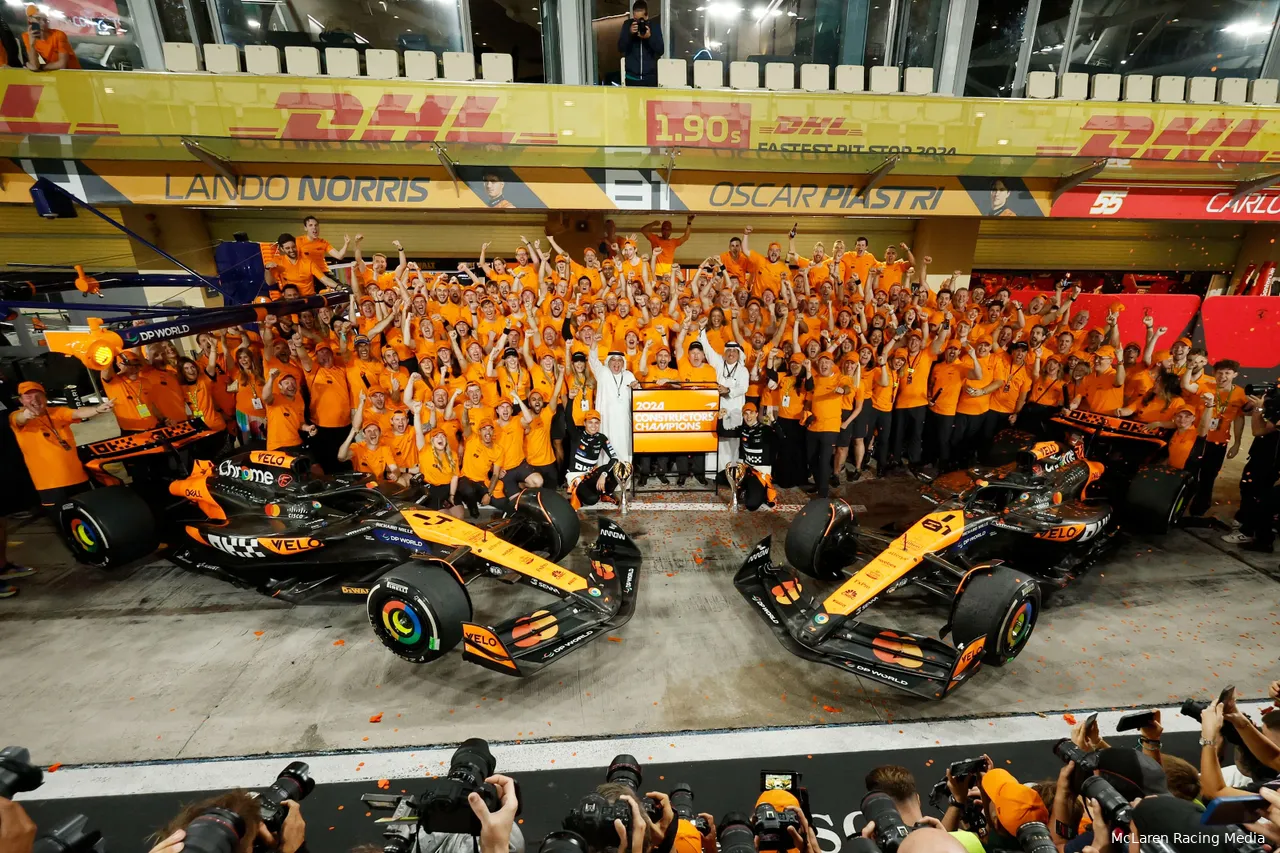 The McLaren Racing team poses for a celebratory photo after securing the 2024 Constructors' title in Abu Dhabi, gathered around both cars in front of their garage.