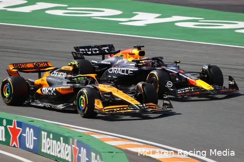 Lando Norris, in a McLaren car, overtaking and driving side by side with Max Verstappen in a Red Bull car at the first corner of Circuit Zandvoort.