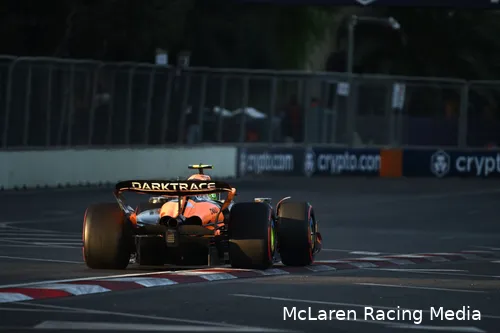 Rear view of Lando Norris's car exiting turn 16 at Baku City Circuit during golden hour, with track barriers in the background.
