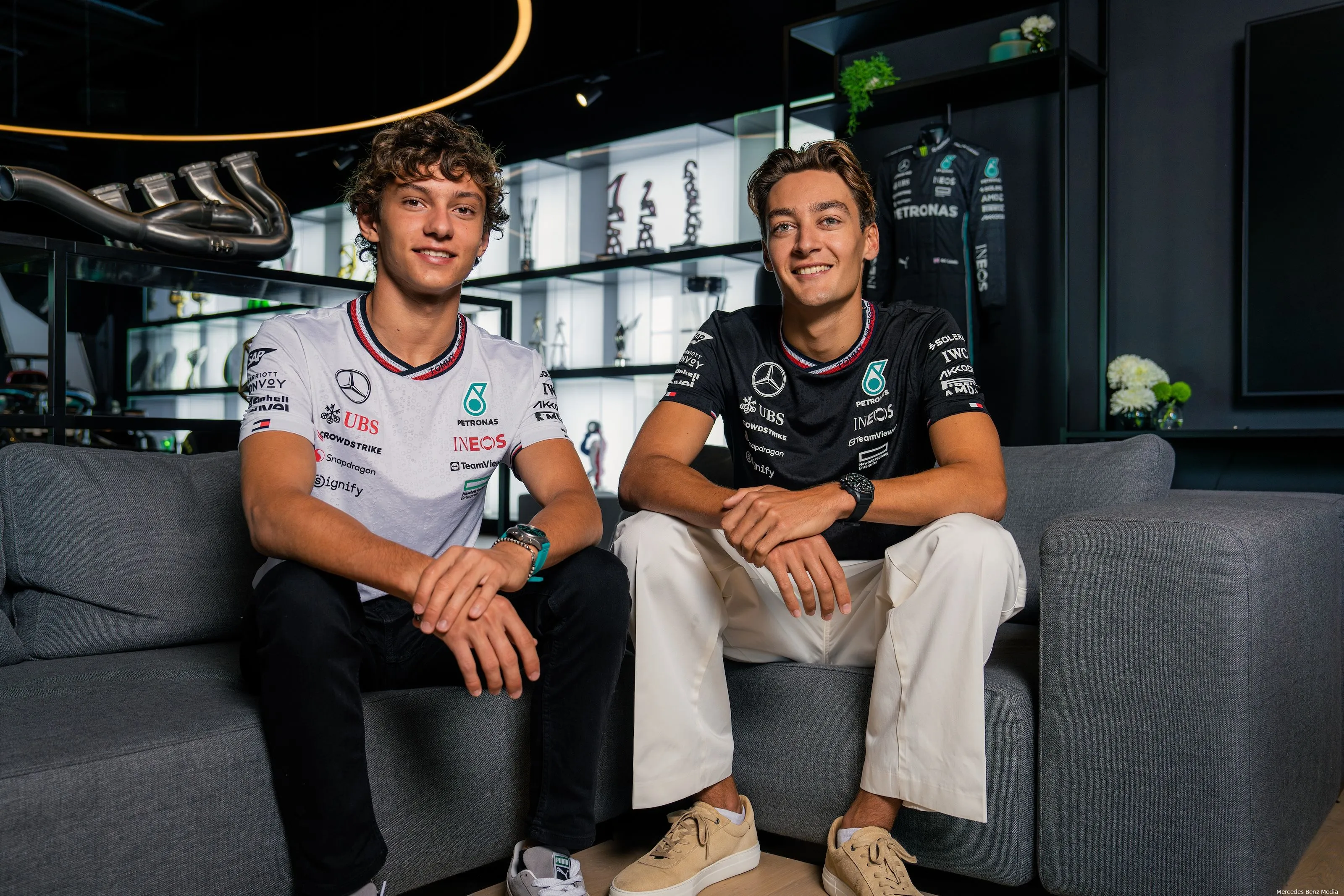 Mercedes 2025 drivers Andrea Kimi Antonelli and George Russell sitting together on a couch, smiling, in the Mercedes hospitality area.