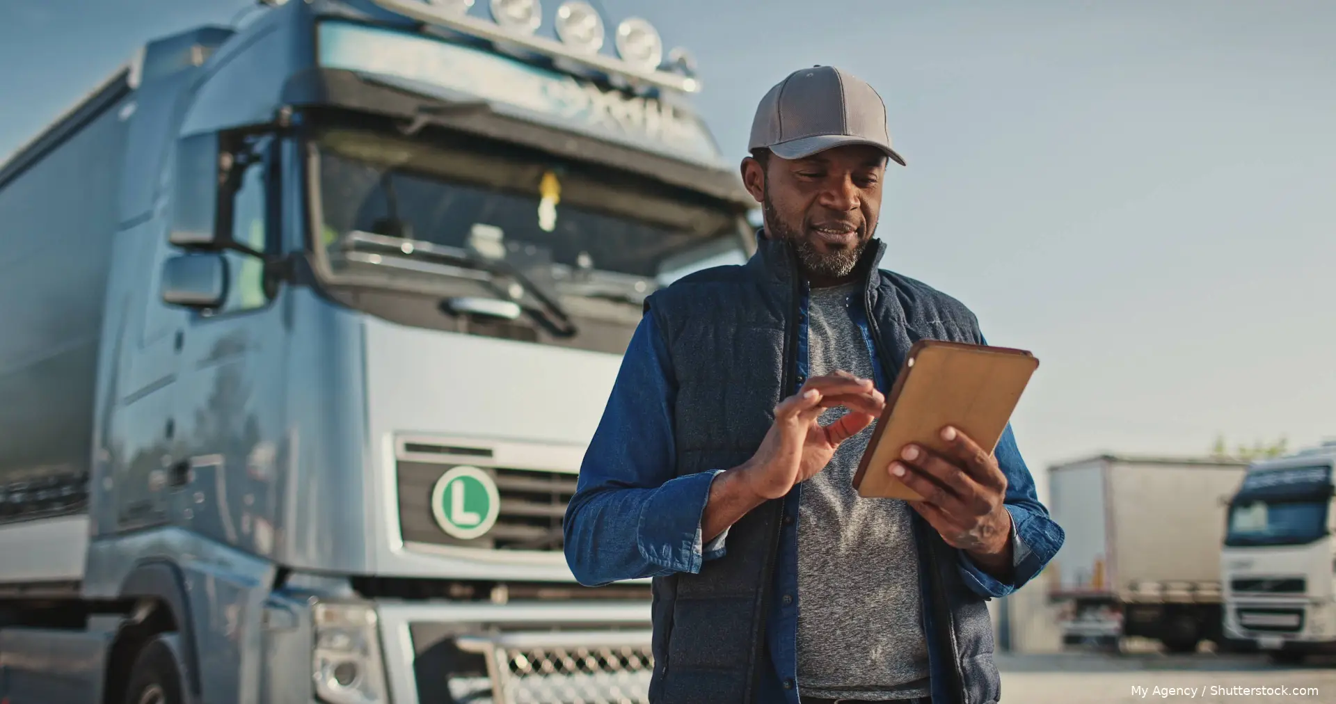 Vrachtwagenchauffeur met pet bekijkt een tablet naast zijn vrachtwagen
