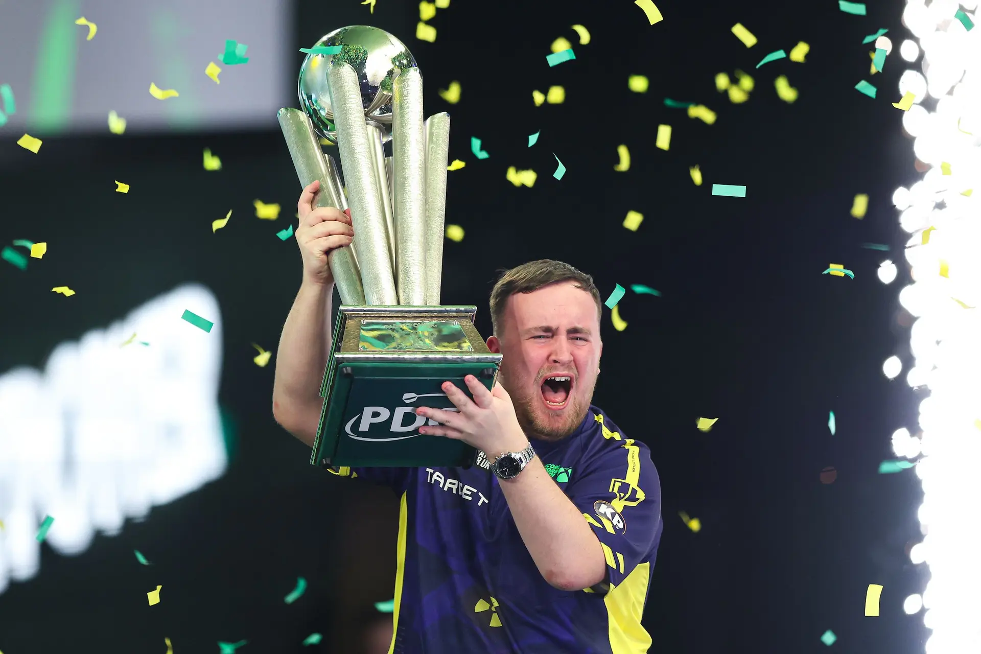 Luke Littler houdt zijn WK-trofee in de lucht.