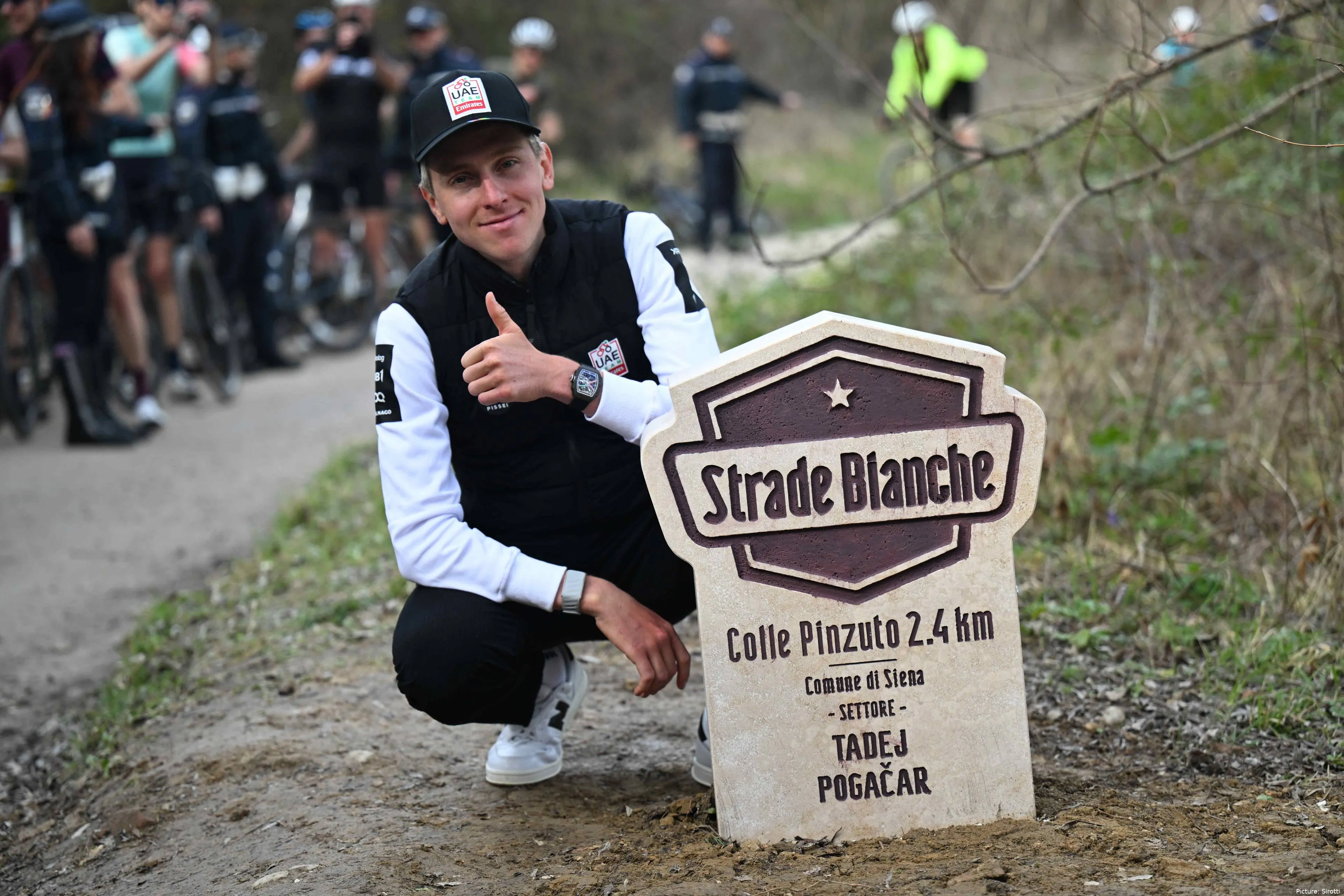 Tadej Pogacar posa junto ao seu marco à beira da estrada antes da Strade Bianche 2026