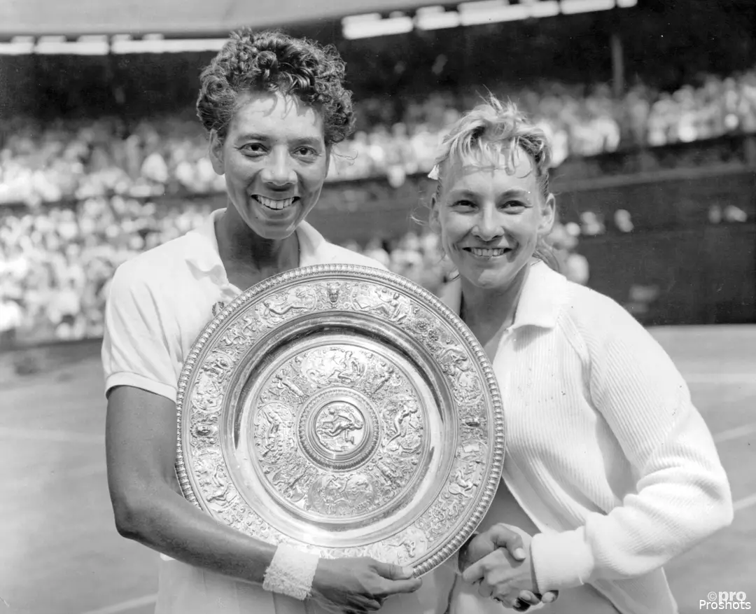 Althea Gibson (izquierda) sosteniendo el trofeo de campeona de Wimbledon en individuales tras vencer a su compatriota Darlene Hard (derecha)