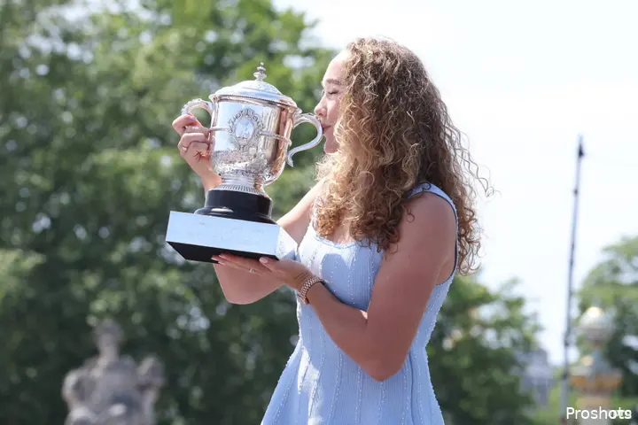 Andreeva, wearing a blue dress, kisses her French Open trophy