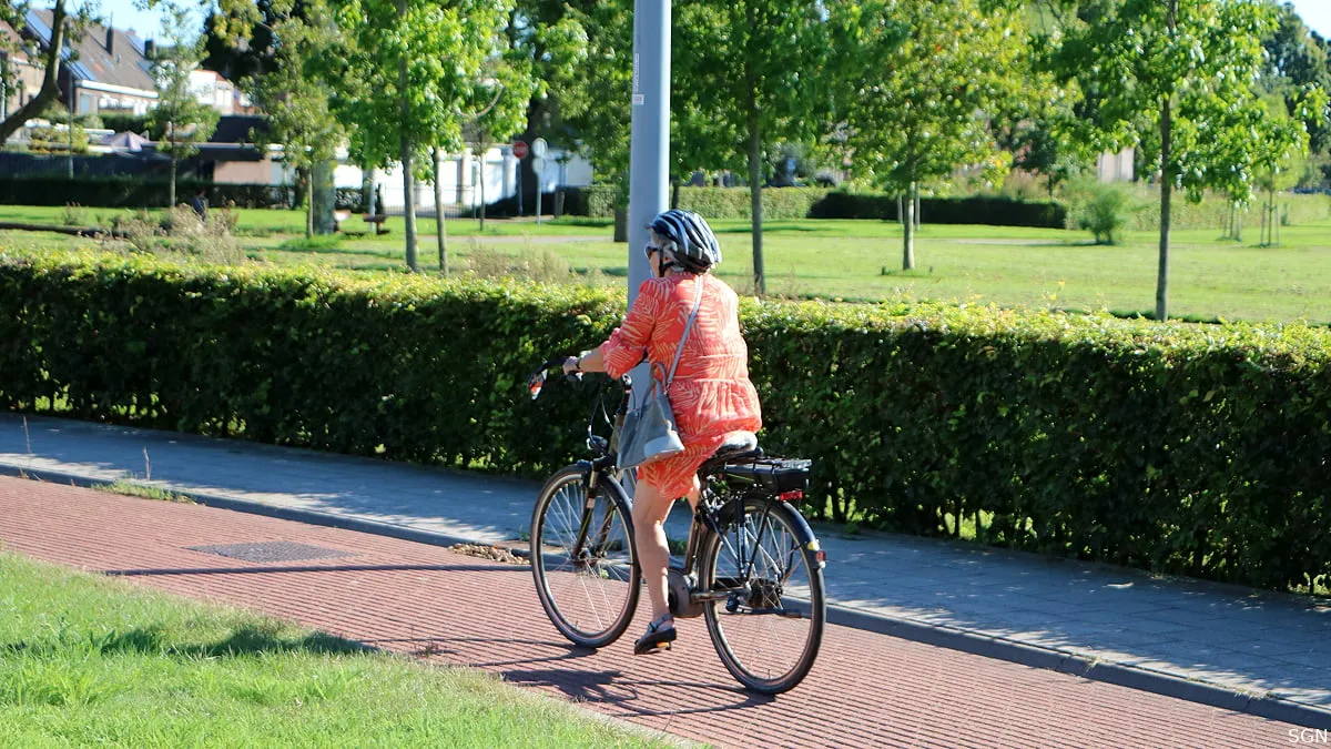 oudere vrouw met fietshelm op elektrische fiets 1