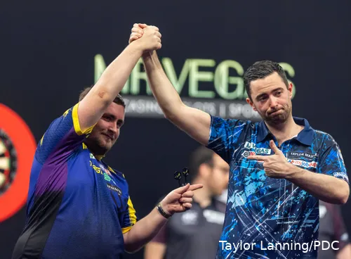 Luke Littler en Luke Humphries wijzen naar elkaar en houden hun handen hoog op het podium.