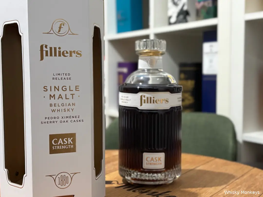 Filliers Cask Strength whisky bottle with box in front of a whisky cabinet and on a whisky cask lid