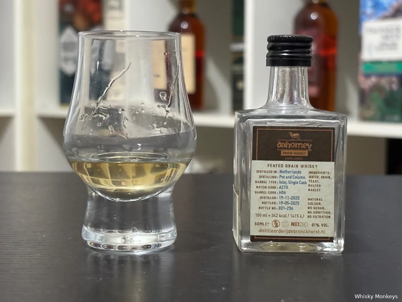 dahomey peated grain fles op een tafel met een glas whisky voor een kast. Specificaties van de grain whisky zijn zichtbaar.